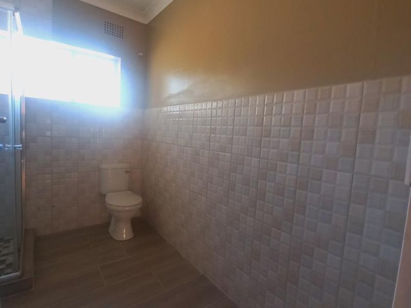 A functional bathroom featuring a shower enclosure, toilet, and neutral tiled finishes throughout.