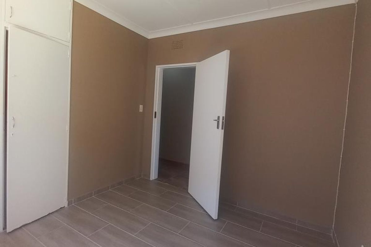 A clean, empty bedroom featuring neutral-toned walls, modern wood-look tiled flooring, and built-in storage cupboards.