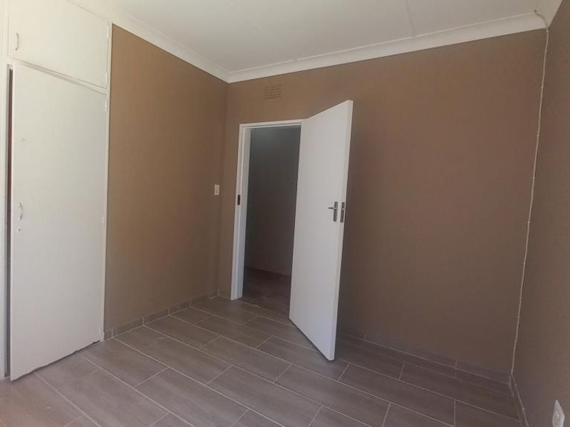 A clean, empty bedroom featuring neutral-toned walls, modern wood-look tiled flooring, and built-in storage cupboards.