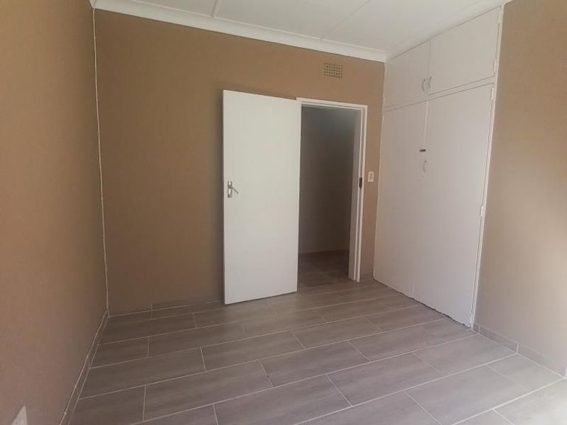 A clean, empty bedroom featuring modern wood-look floor tiles, neutral wall paint, and built-in storage cupboards.