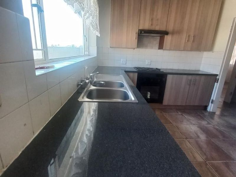 A functional kitchen featuring laminate cabinetry, granite countertops, a stainless steel double sink, and built-in cooking appliances with tiled flooring and splashbacks.