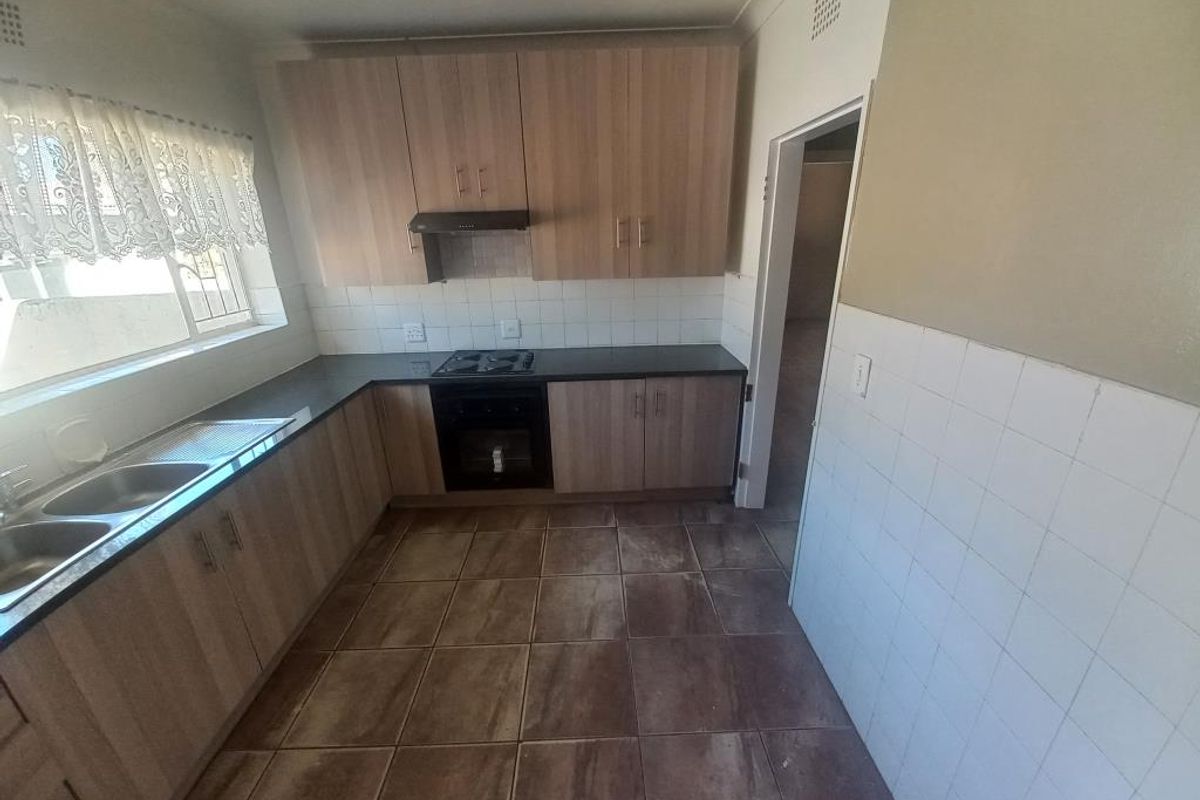 A functional kitchen featuring laminate cabinetry, built-in oven and hob, extractor fan, and tiled flooring, offering a clean and practical workspace.