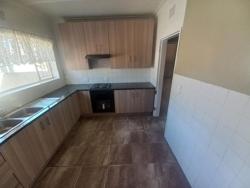 A functional kitchen featuring laminate cabinetry, built-in oven and hob, extractor fan, and tiled flooring, offering a clean and practical workspace.
