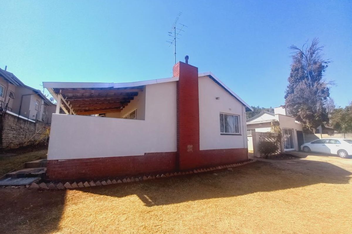 Rear view of the house featuring a brick chimney, a covered patio area with exposed timber rafters, and a surrounding garden space.