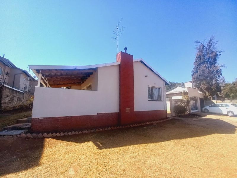 Rear view of the house featuring a brick chimney, a covered patio area with exposed timber rafters, and a surrounding garden space.