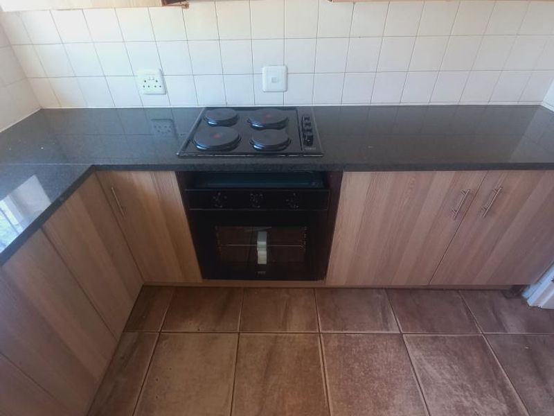 A functional kitchen featuring laminate cabinetry, granite countertops, a built-in oven, electric hob, and extractor fan with tiled backsplash and flooring.