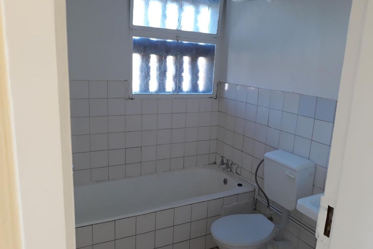 A dated bathroom featuring a standard bathtub, toilet, and tiled finishes, requiring modernization and cosmetic updates to improve its overall condition.