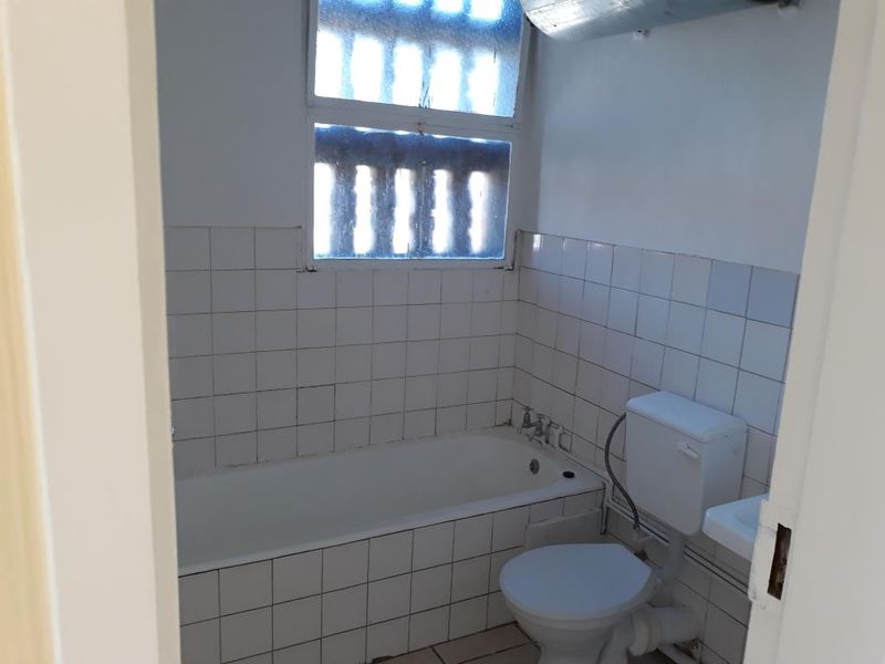 A dated bathroom featuring a standard bathtub, toilet, and tiled finishes, requiring modernization and cosmetic updates to improve its overall condition.