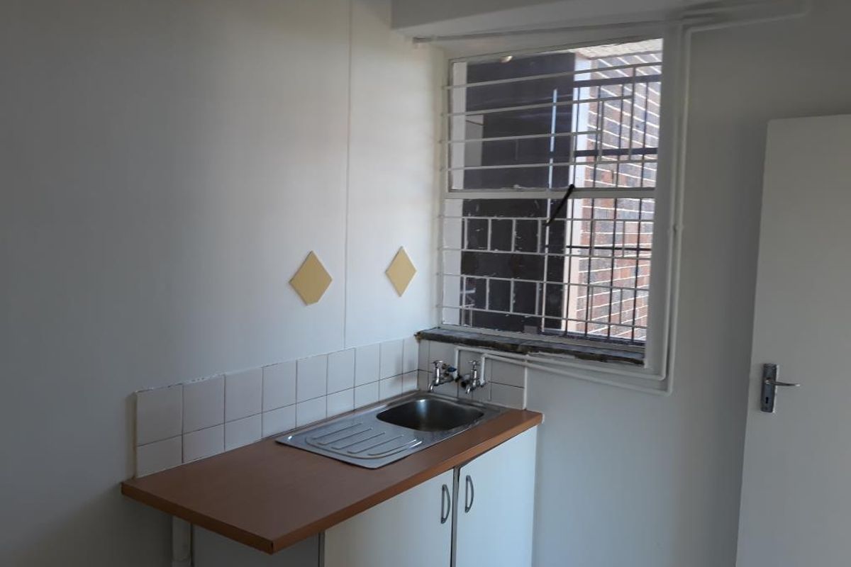 A compact kitchen area featuring a single stainless steel sink, laminate countertop, base cabinetry, and a window fitted with security bars.