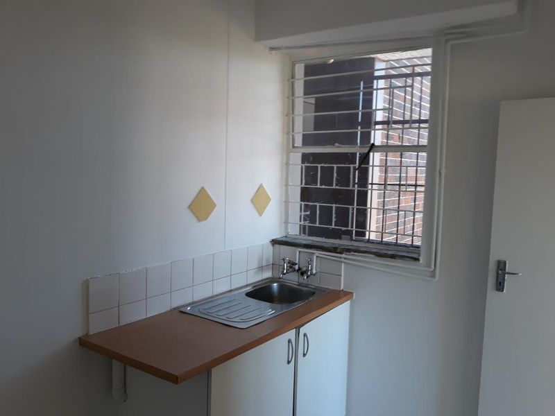 A compact kitchen area featuring a single stainless steel sink, laminate countertop, base cabinetry, and a window fitted with security bars.