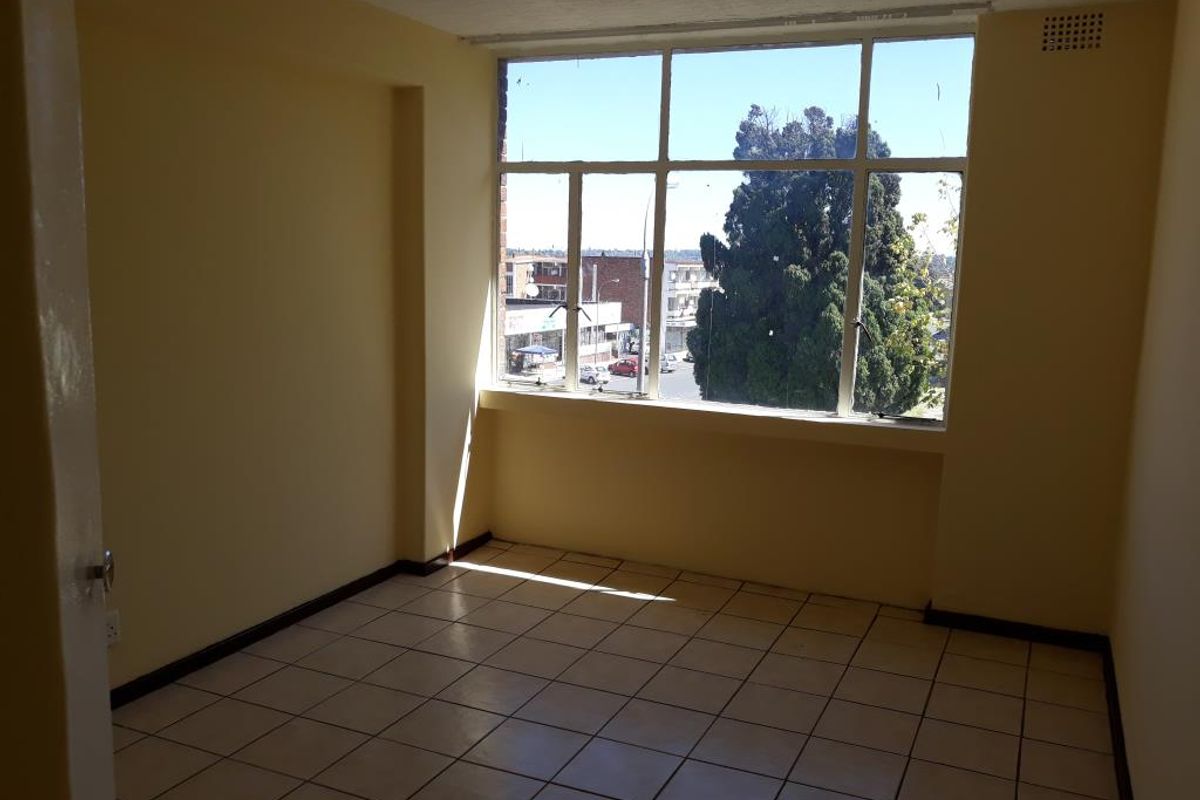 An empty living room featuring large windows with natural light, tiled flooring, and neutral wall finishes, offering a blank canvas for interior design.