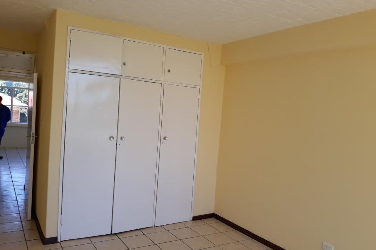 A clean, empty bedroom featuring tiled flooring and white built-in cupboards with overhead storage compartments.