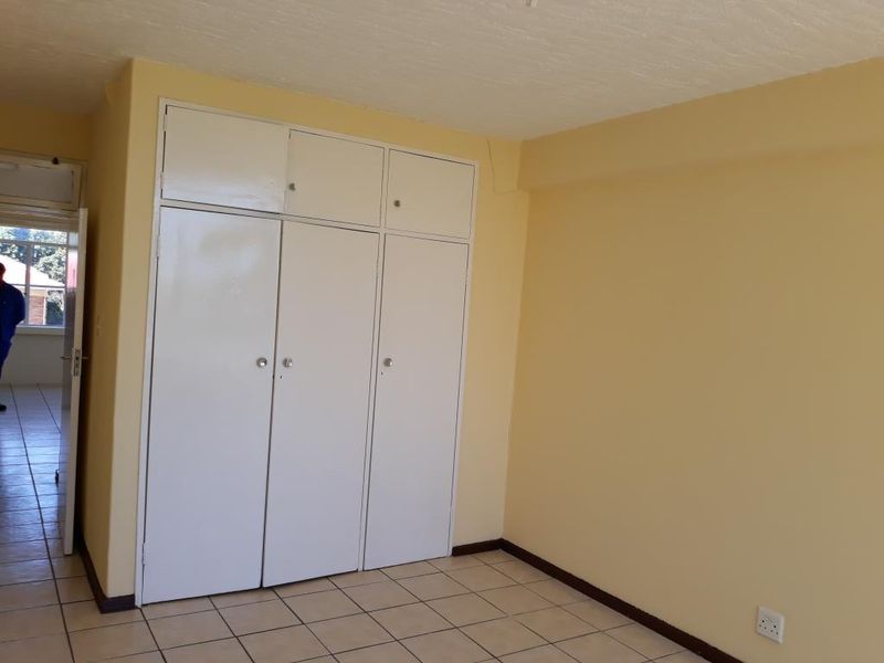 A clean, empty bedroom featuring tiled flooring and white built-in cupboards with overhead storage compartments.