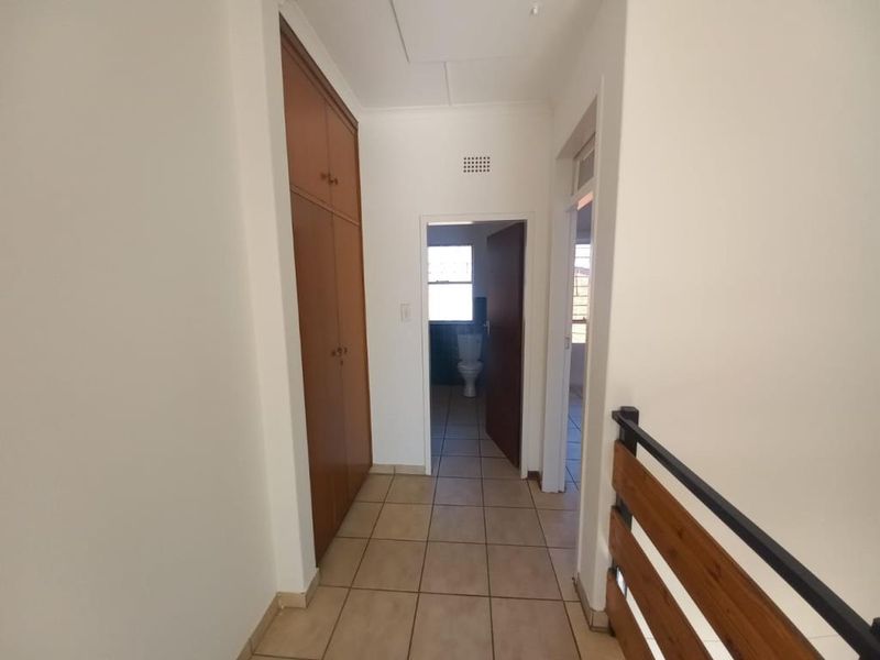 A functional hallway featuring tiled flooring, built-in wooden cupboards for storage, and a timber balustrade, providing access to adjacent rooms.