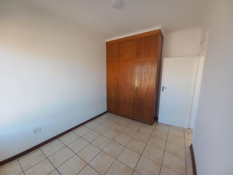 A clean, empty bedroom featuring tiled flooring and a large, built-in wooden wardrobe providing ample storage space.