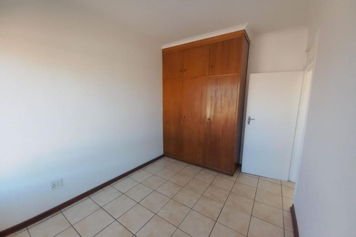 A clean, empty bedroom featuring tiled flooring and a large, built-in wooden wardrobe providing ample storage space.