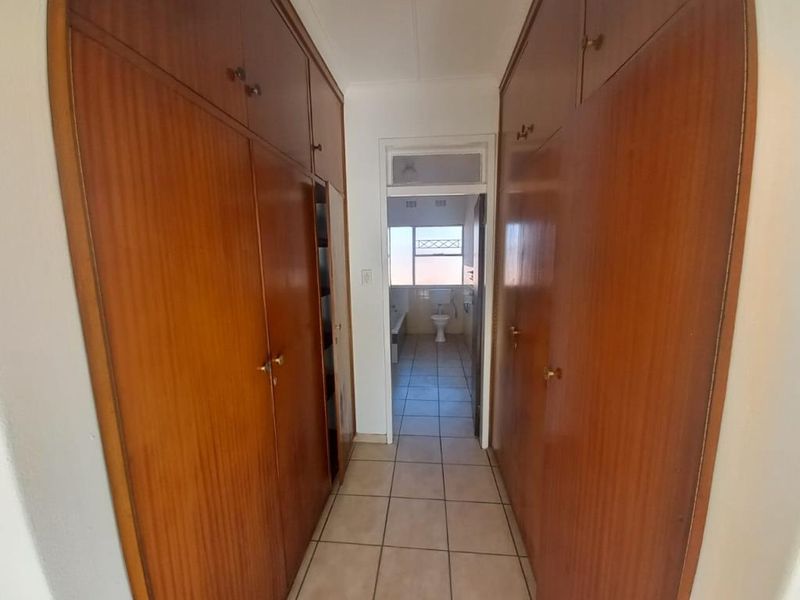 A functional hallway featuring extensive floor-to-ceiling built-in wooden cupboards and tiled flooring, providing direct access to the adjacent bathroom.