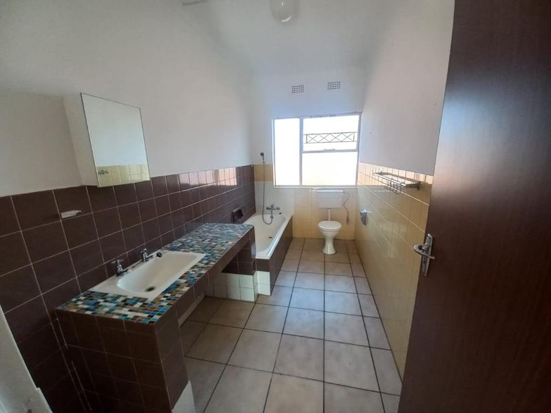 A dated bathroom featuring a built-in vanity, bathtub, and toilet with tiled finishes throughout, offering potential for modernization and renovation.