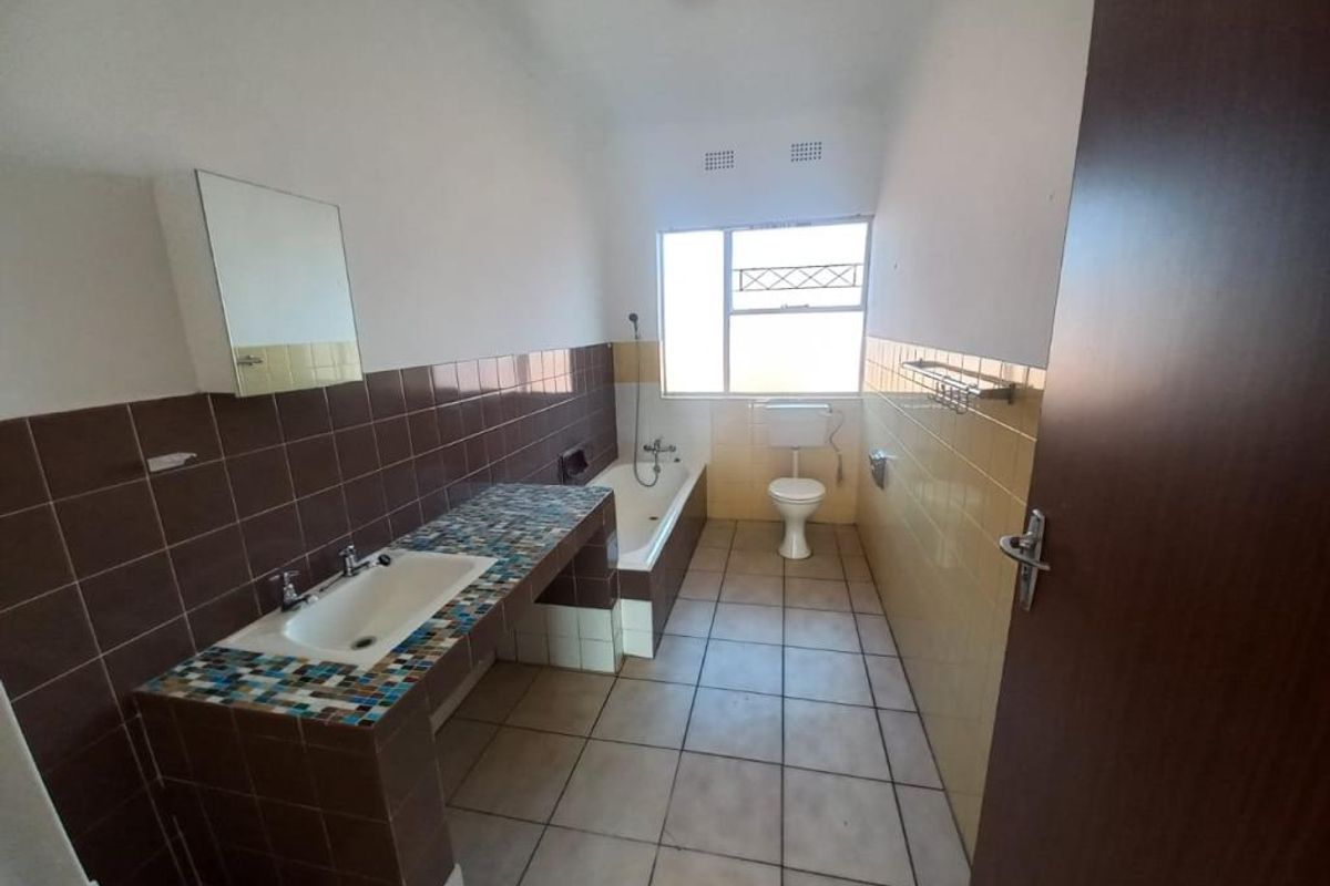 A dated bathroom featuring a built-in vanity, bathtub, and toilet with tiled finishes throughout, offering potential for modernization and renovation.