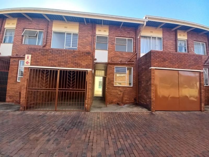 Front elevation of a face brick apartment complex featuring a paved driveway, secure metal gates, and a private garage.