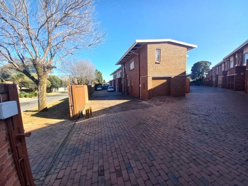 Exterior view of the apartment complex featuring a brick facade, paved driveway, and secure gated entrance with individual garage access.