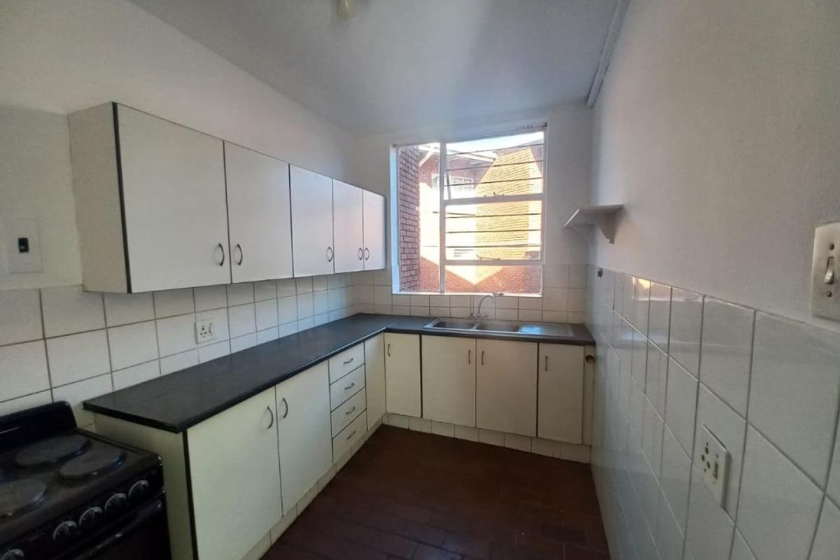 Functional kitchen featuring white cabinetry, dark laminate countertops, double sink, tiled backsplash, and ceramic flooring with a freestanding stove.