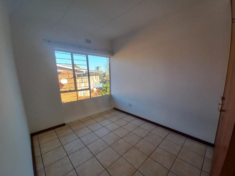 A vacant bedroom featuring tiled flooring, a large window with security bars, and a built-in cupboard.