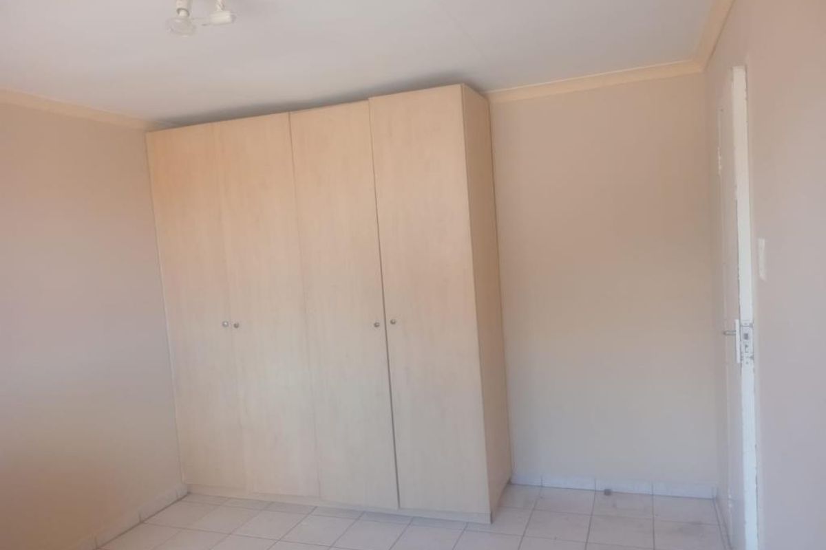 A vacant bedroom featuring neutral tiled flooring, a built-in wardrobe, and basic ceiling lighting, offering a blank canvas for personalization.