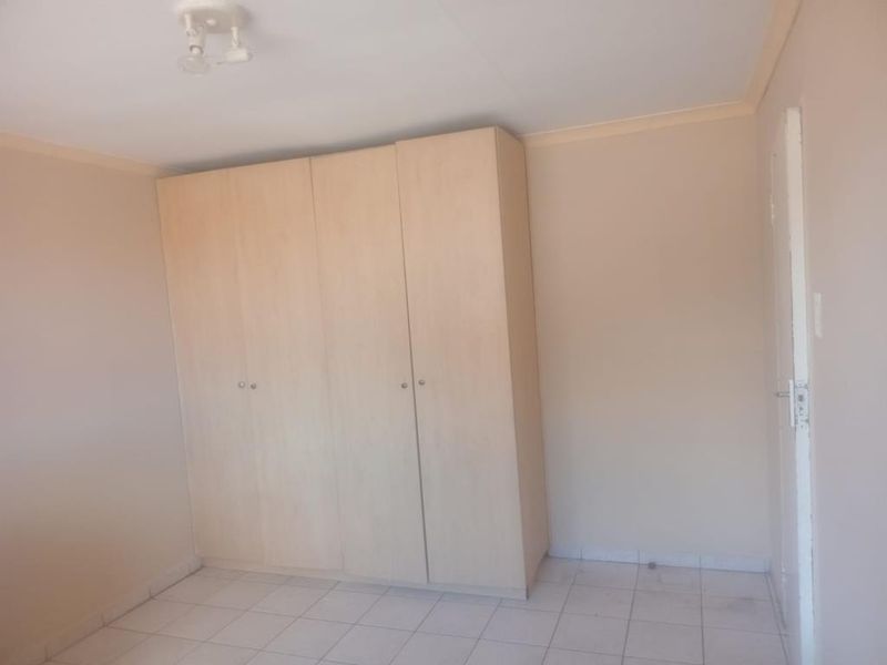 A vacant bedroom featuring neutral tiled flooring, a built-in wardrobe, and basic ceiling lighting, offering a blank canvas for personalization.