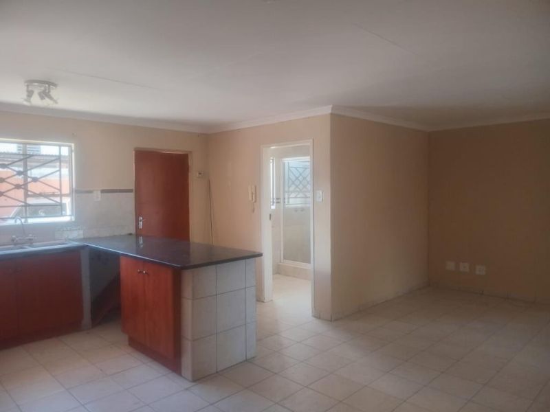 Open plan living and kitchen area featuring tiled flooring, built-in cabinetry with laminate countertops, and direct access to an adjacent room.