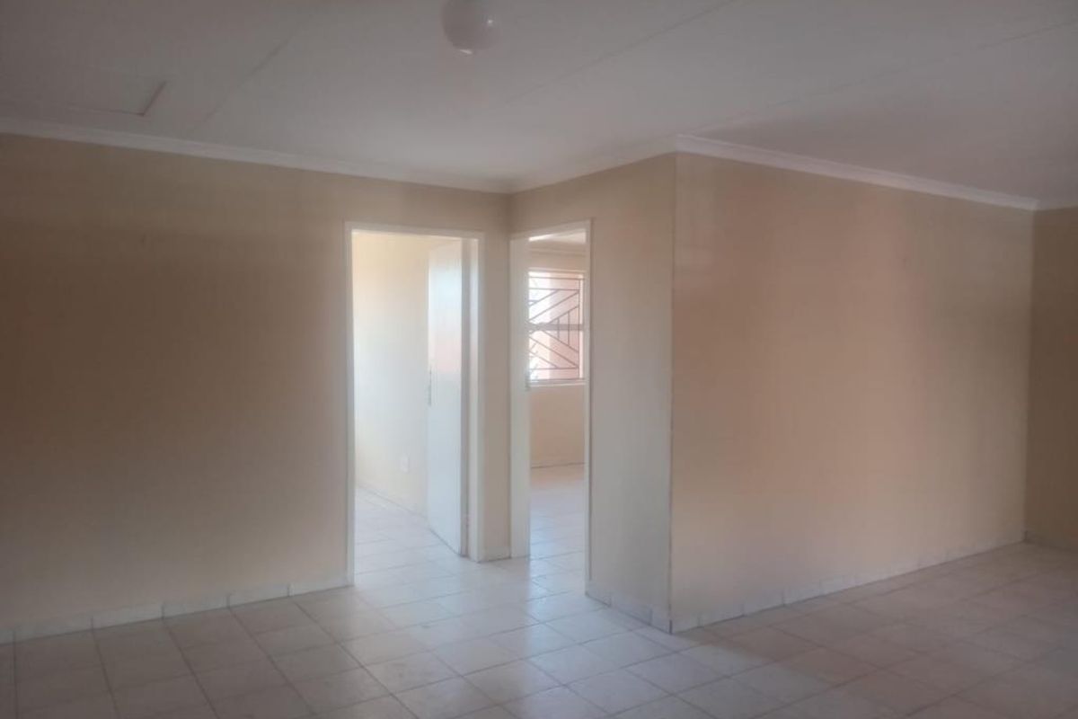 An empty, neutrally painted living area featuring tiled flooring and access to adjacent rooms through standard doorways.