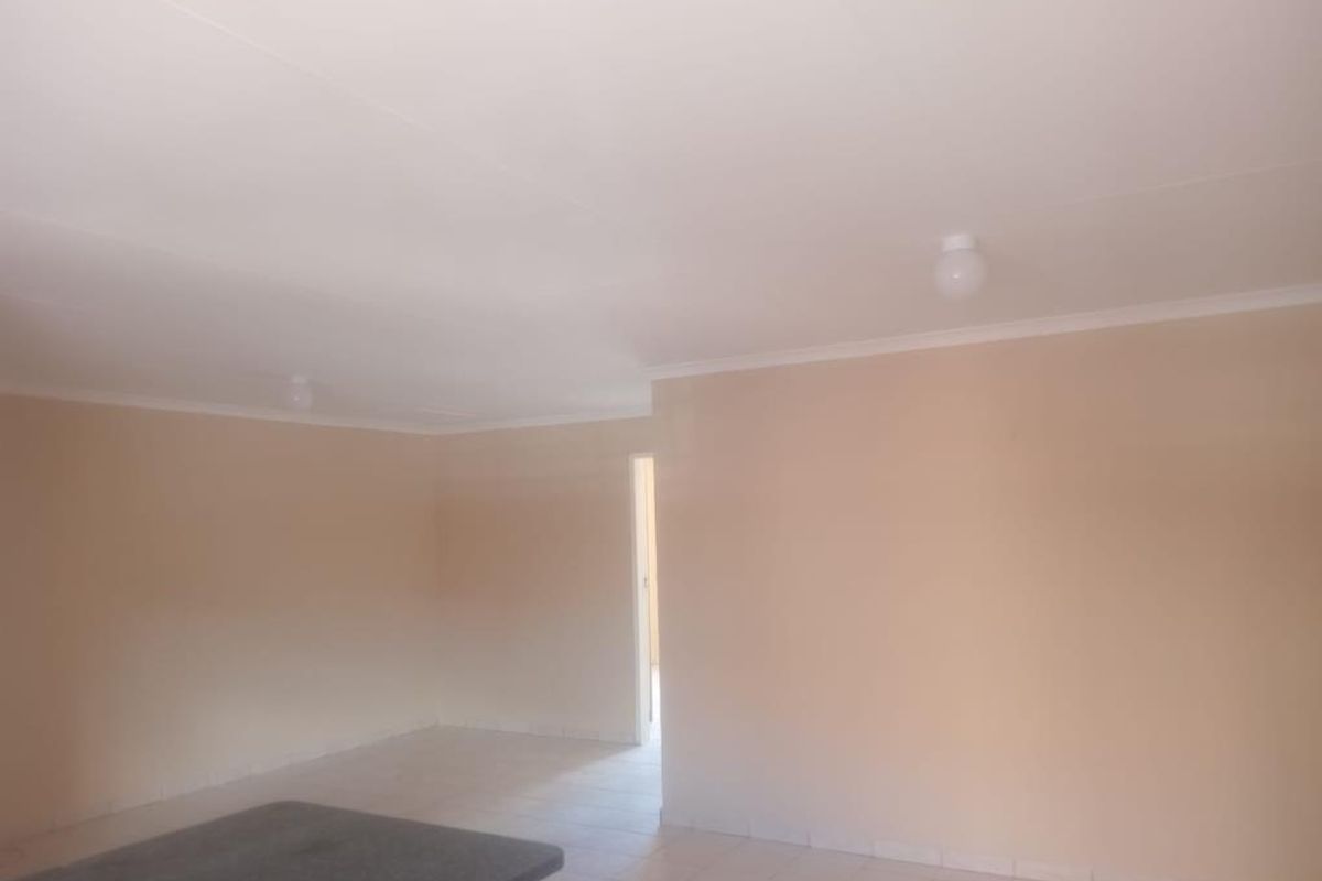 An empty open-plan living area featuring neutral wall paint, tiled flooring, and simple ceiling lighting, offering a blank canvas for interior design.