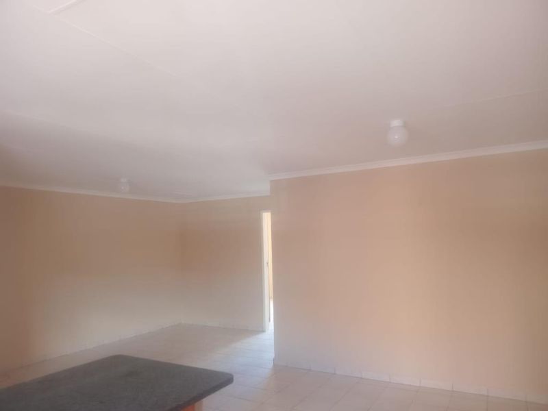 An empty open-plan living area featuring neutral wall paint, tiled flooring, and simple ceiling lighting, offering a blank canvas for interior design.