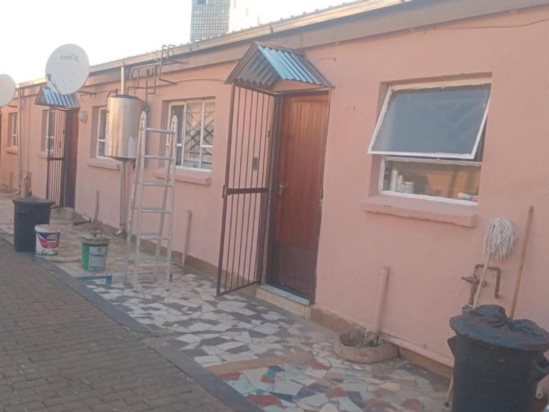 Exterior view of the rear apartment facade featuring a security gate, awning, and paved walkway area.