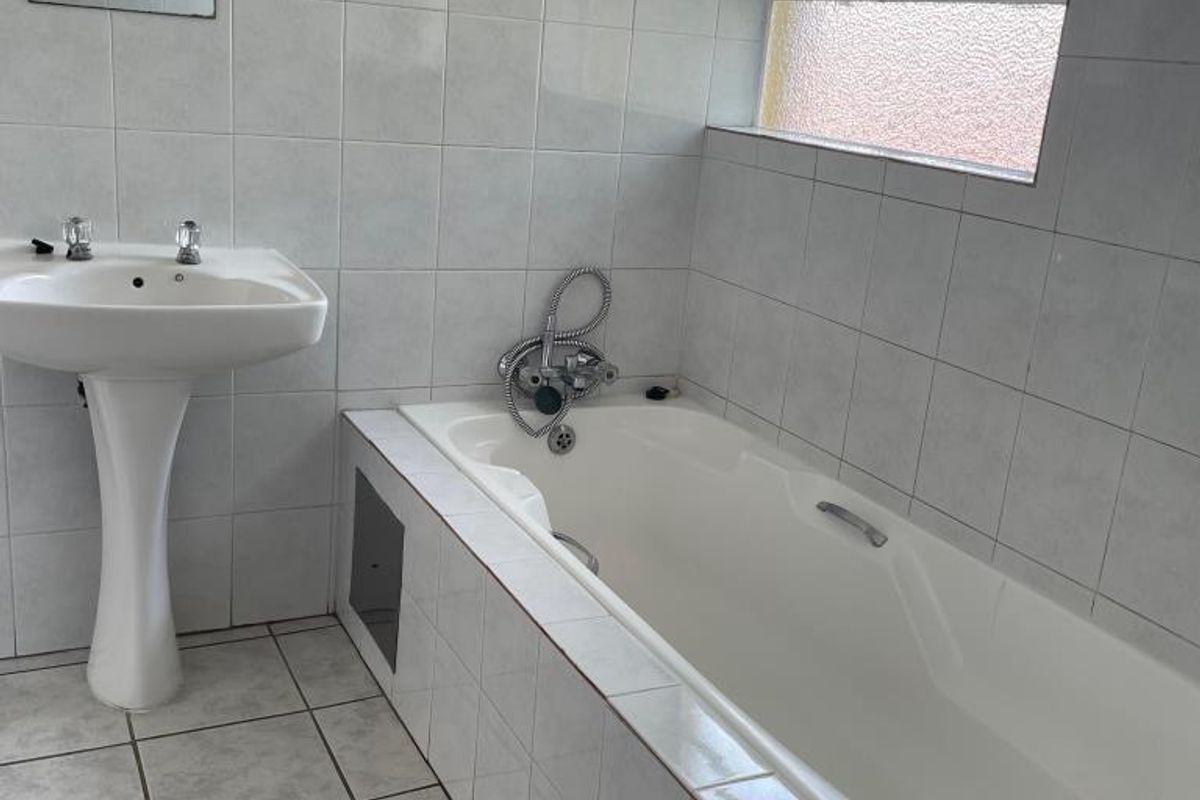A functional bathroom featuring a pedestal basin, a built-in bathtub with tiled surround, and neutral wall and floor tiling.