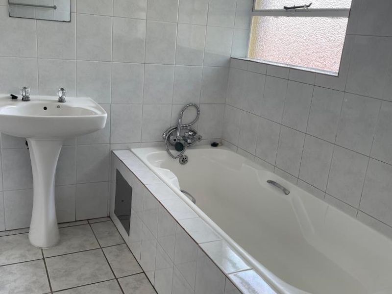 A functional bathroom featuring a pedestal basin, a built-in bathtub with tiled surround, and neutral wall and floor tiling.