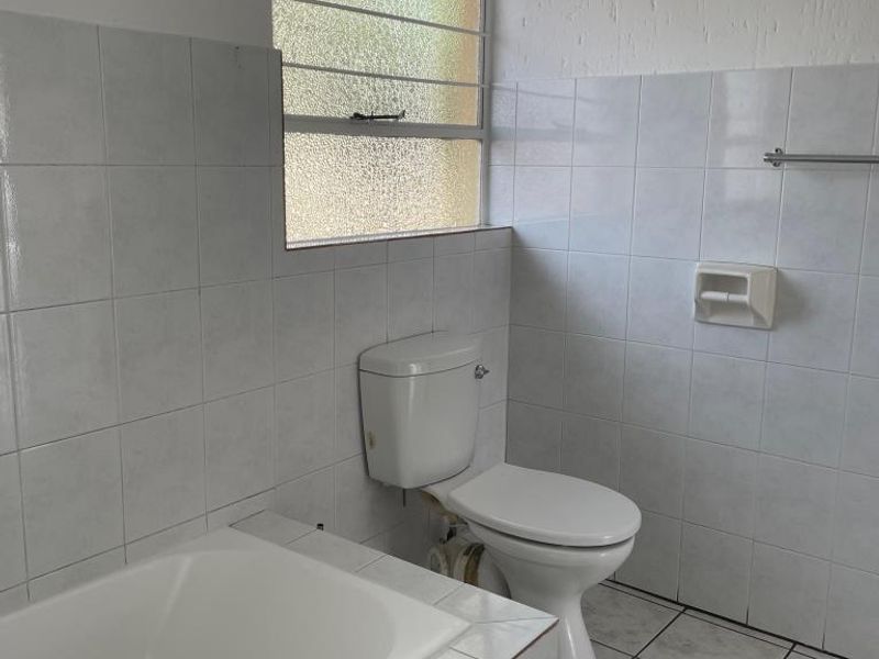 A dated bathroom featuring a built-in bathtub, toilet, and tiled finishes, offering a blank canvas for renovation and modernization.