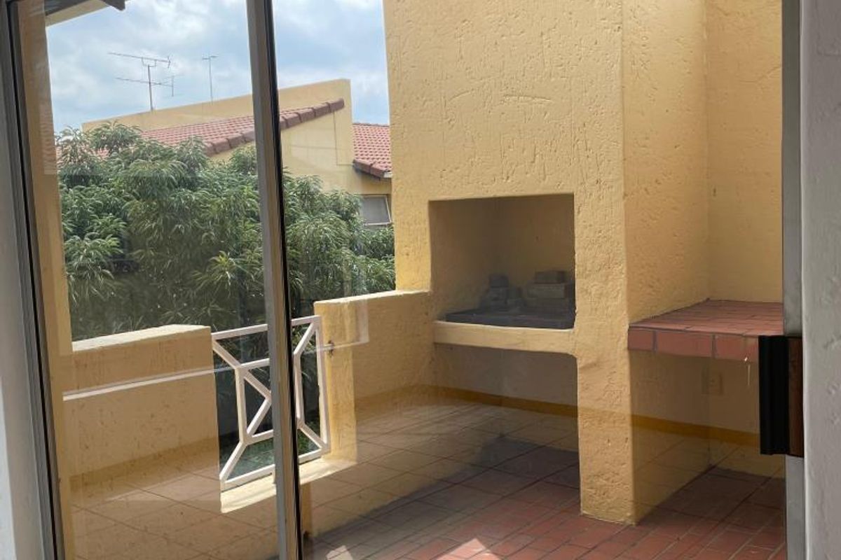 A covered balcony featuring a built-in braai, terracotta tiled flooring, and a sliding glass door providing access to the living area.