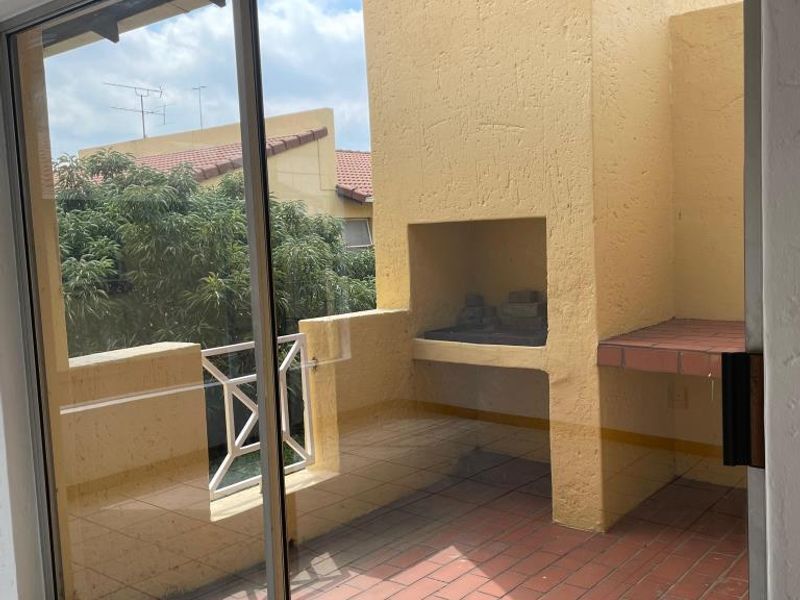 A covered balcony featuring a built-in braai, terracotta tiled flooring, and a sliding glass door providing access to the living area.