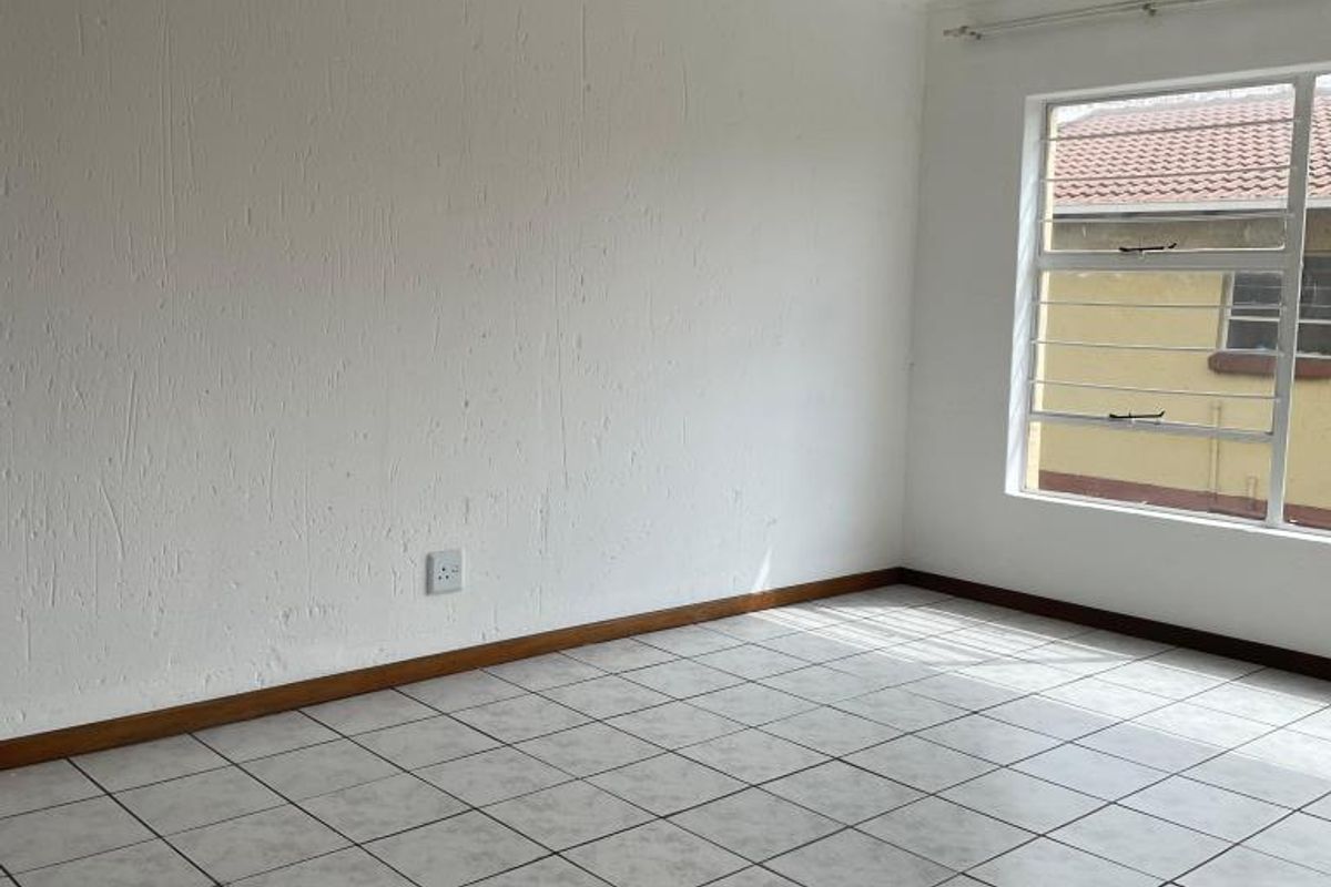 A bright, empty bedroom featuring neutral tiled flooring, white walls, and a window fitted with security bars.