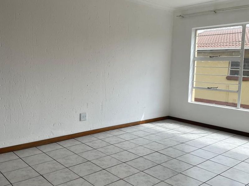 A bright, empty bedroom featuring neutral tiled flooring, white walls, and a window fitted with security bars.