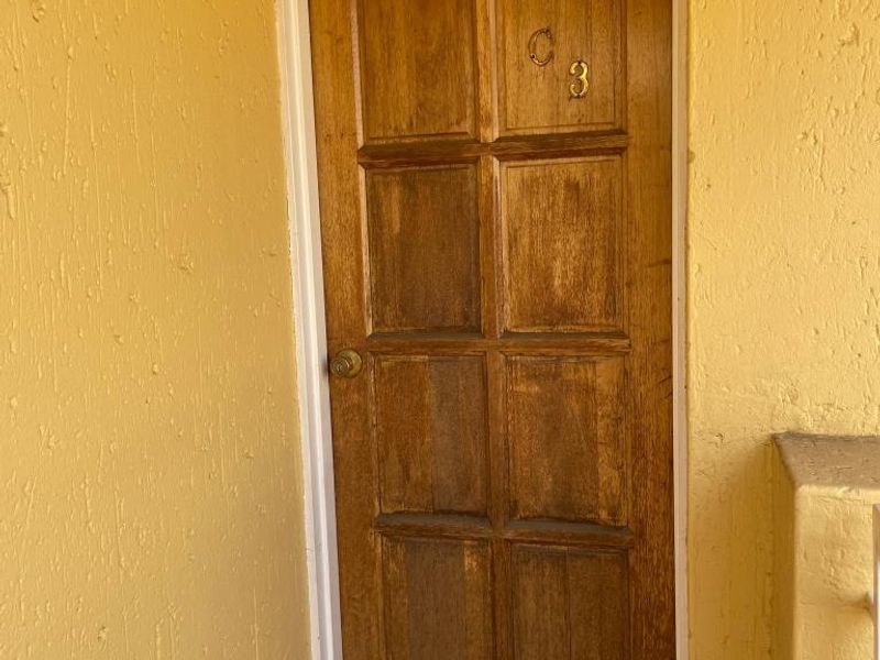 Exterior view of a wooden apartment entrance door with a tiled threshold and yellow textured wall finish.