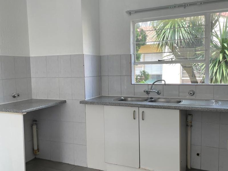 A functional kitchen area featuring a double sink, tiled splashback, laminate countertops, and base cabinetry, with tiled flooring throughout.