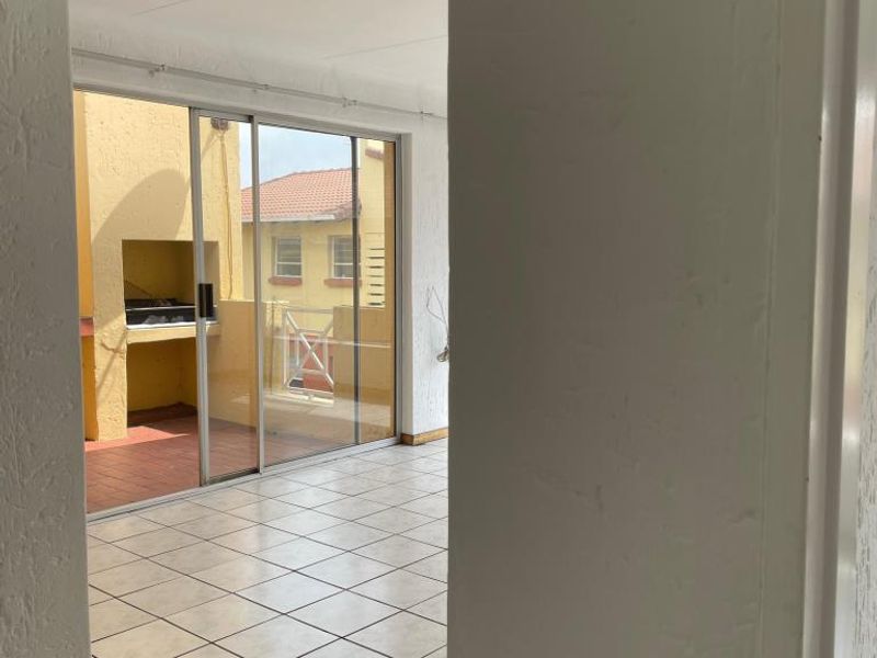 An open-plan living area featuring tiled floors and sliding doors that open onto a balcony with a built-in braai.