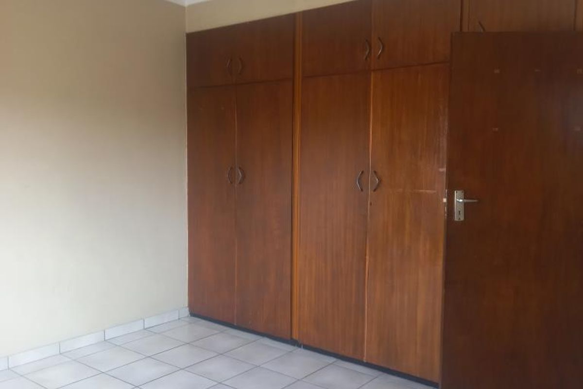 An empty bedroom featuring tiled flooring and extensive built-in wooden cupboards, offering ample storage space.