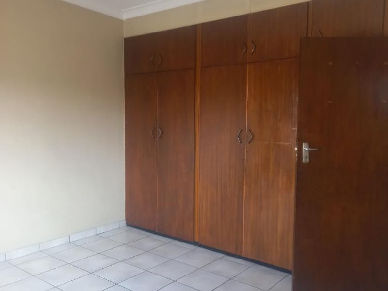 An empty bedroom featuring tiled flooring and extensive built-in wooden cupboards, offering ample storage space.