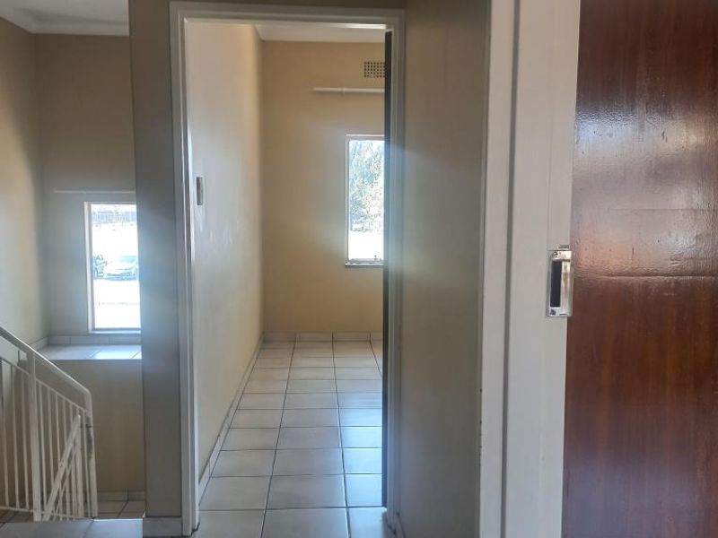 A functional hallway featuring tiled flooring, a staircase railing, and neutral wall finishes, providing access to adjacent living spaces.