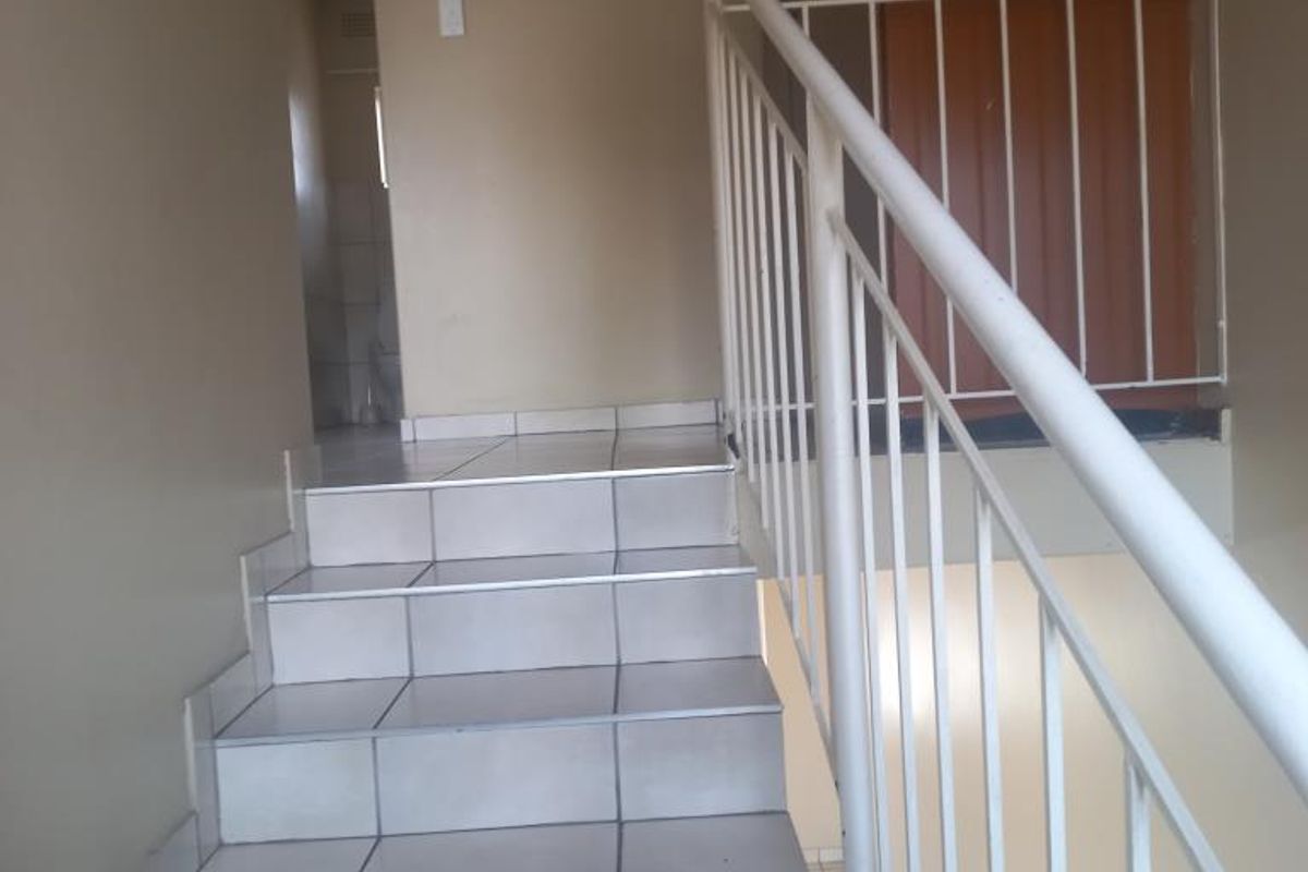 A functional hallway featuring a tiled staircase with a white metal balustrade and a built-in storage cupboard.