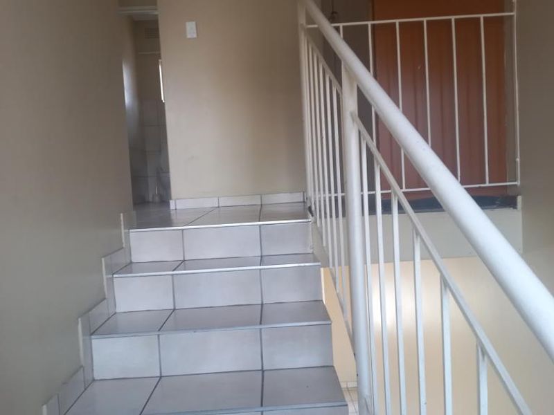 A functional hallway featuring a tiled staircase with a white metal balustrade and a built-in storage cupboard.