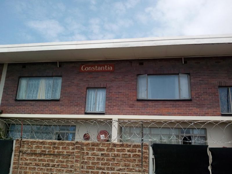 Exterior view of the Constantia apartment building featuring a face brick facade, casement windows, and a secure boundary wall with razor wire.